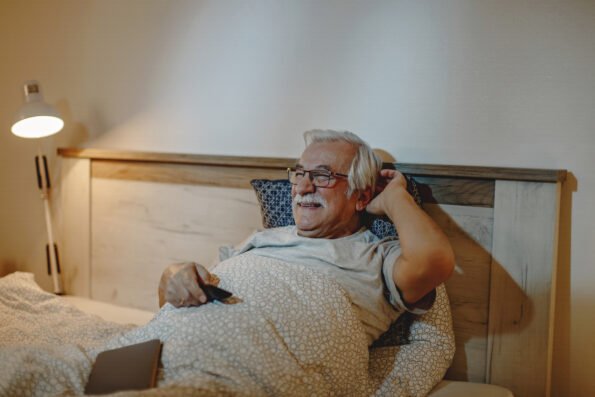 Happy mature man enjoying while watching TV in bed at night.